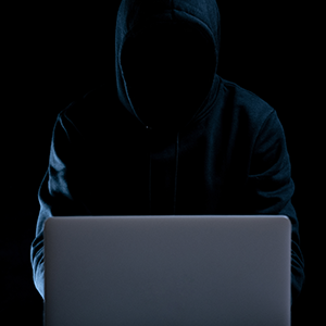 silhouetted person wearing a hood with a laptop